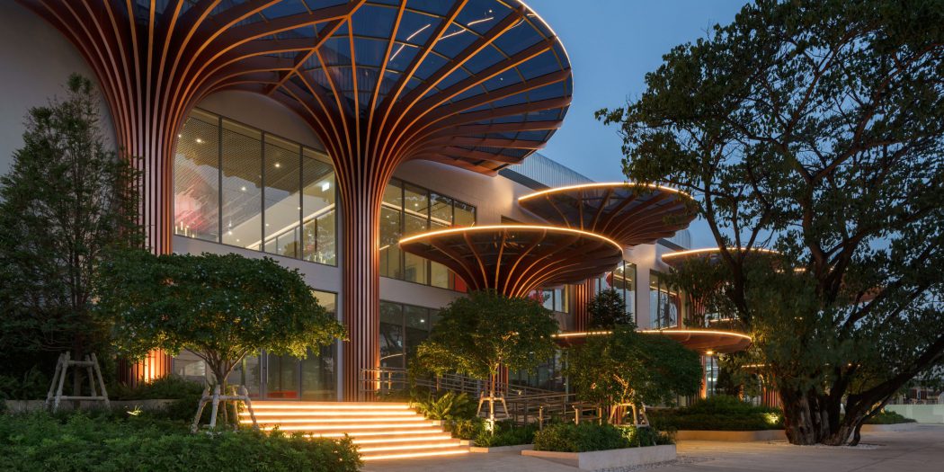 Exterior twilight view of the NAP+ Factory building by OPNBX featuring illuminated tree-like canopy columns and landscaped entry steps.
