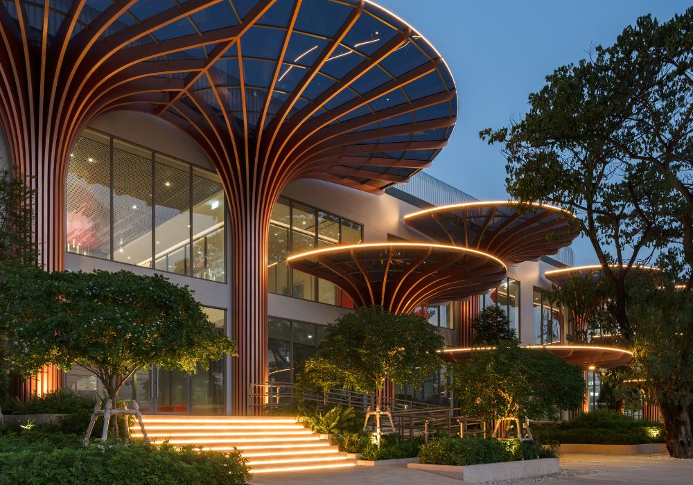 Modern biophilic architecture featuring illuminated tree-canopy roof structures and warm LED lighting at dusk.